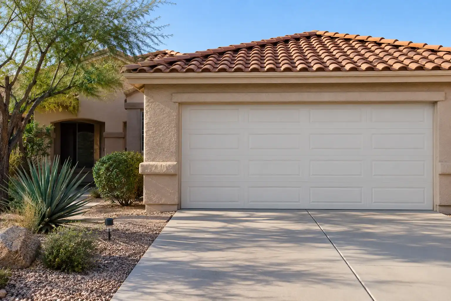 Stucco home with a red tile roof and a white raised panel two car garage door